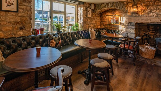 A cozy pub with stone walls, leather seating, wooden tables, and a fireplace. - The Bowl Inn (Bristol)