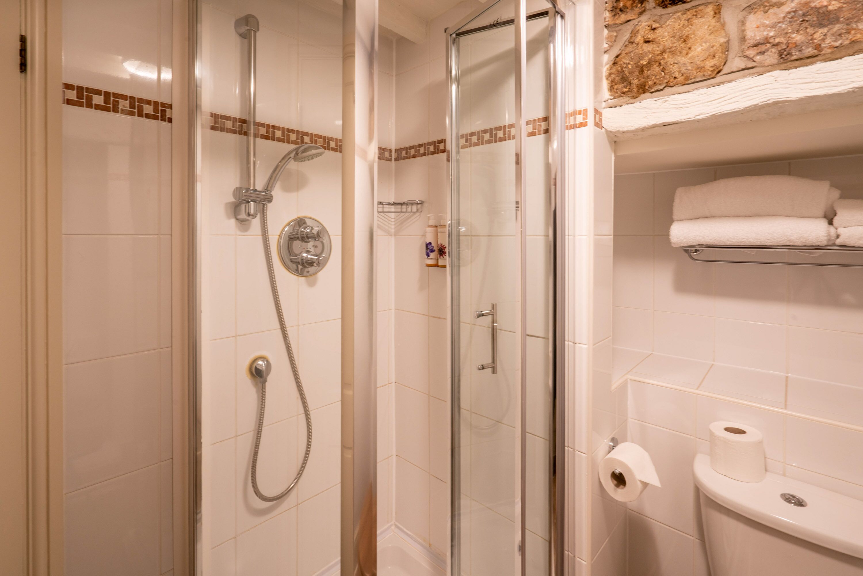 Un baño con ducha envuelta en vidrio, inodoro y estante con toallas.