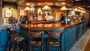 A bar area with wooden bar counter, multiple bar stools, and overhead lighting fixtures. - The Bowl Inn (Bristol)