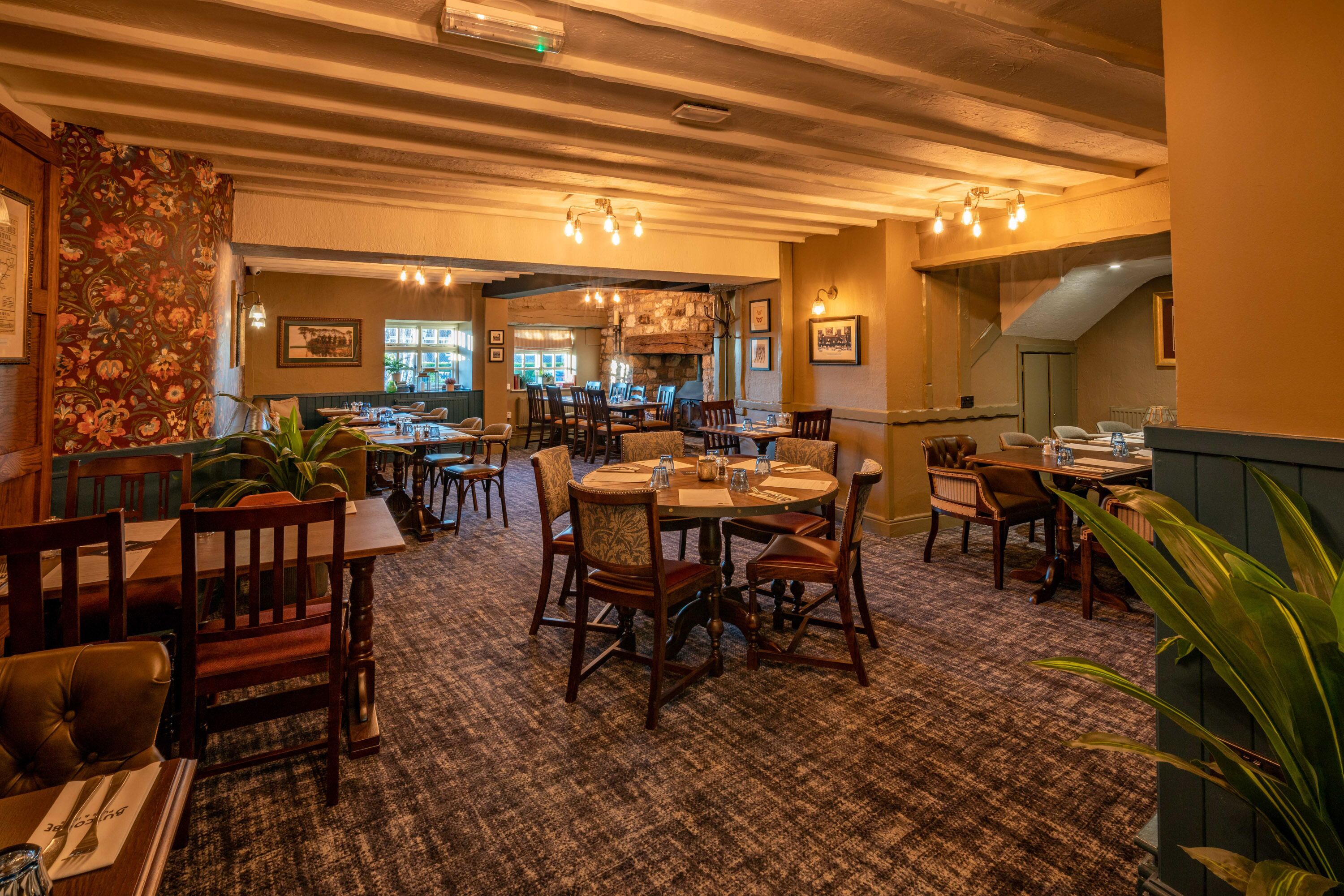 A restaurant with wooden tables and chairs, carpeted floor, and a stone wall.