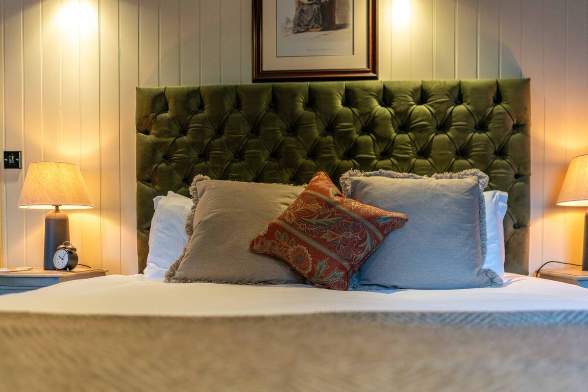 A neatly made bed with a tufted headboard, two bedside lamps, and a framed picture above the headboard.