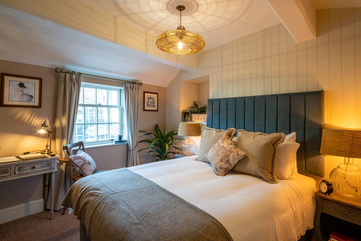 A well-lit bedroom with a large bed, a desk, and a window with curtains.