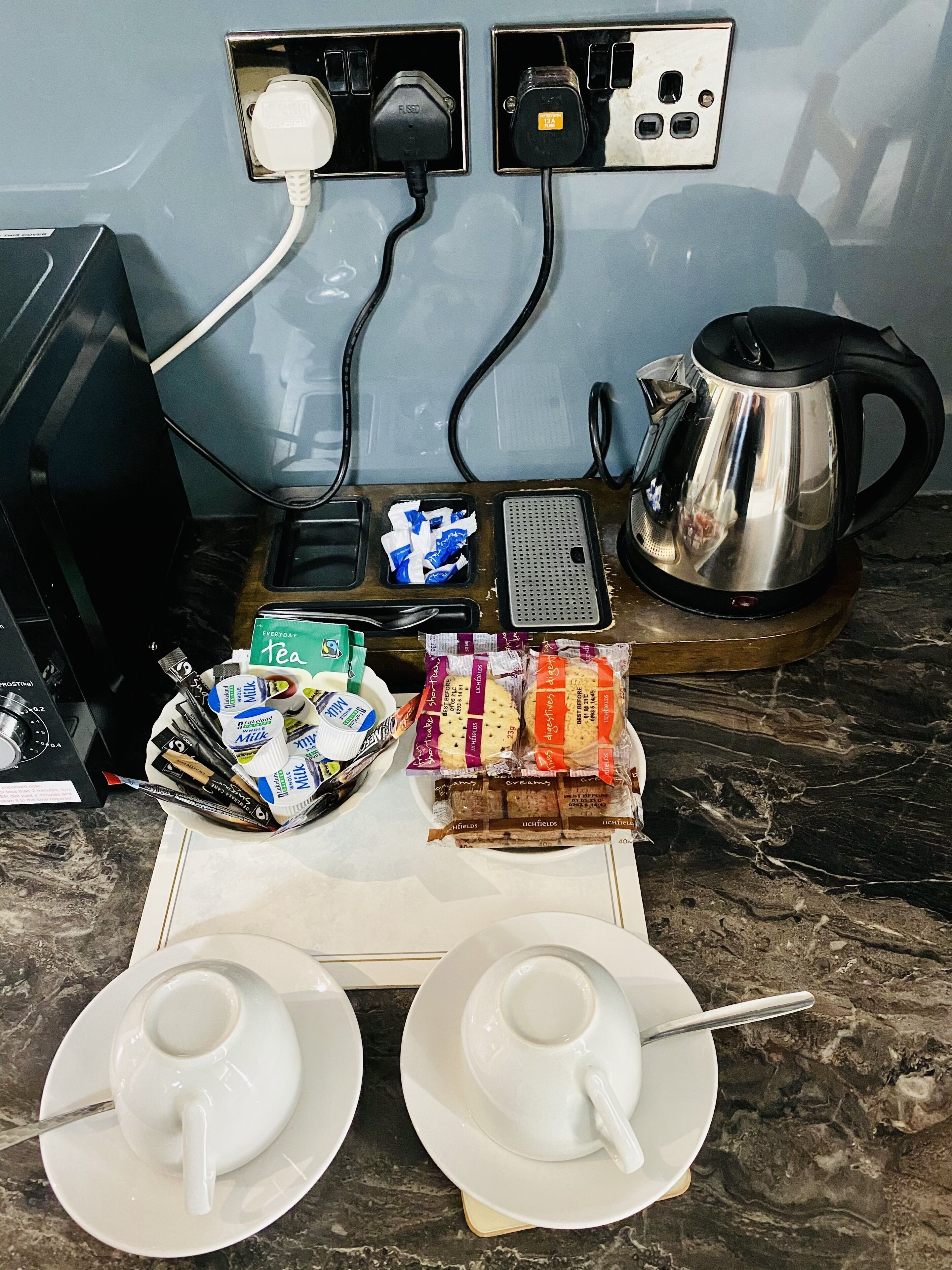 A kitchen counter with a kettle, a coffee maker, and a tray of tea and biscuits.
