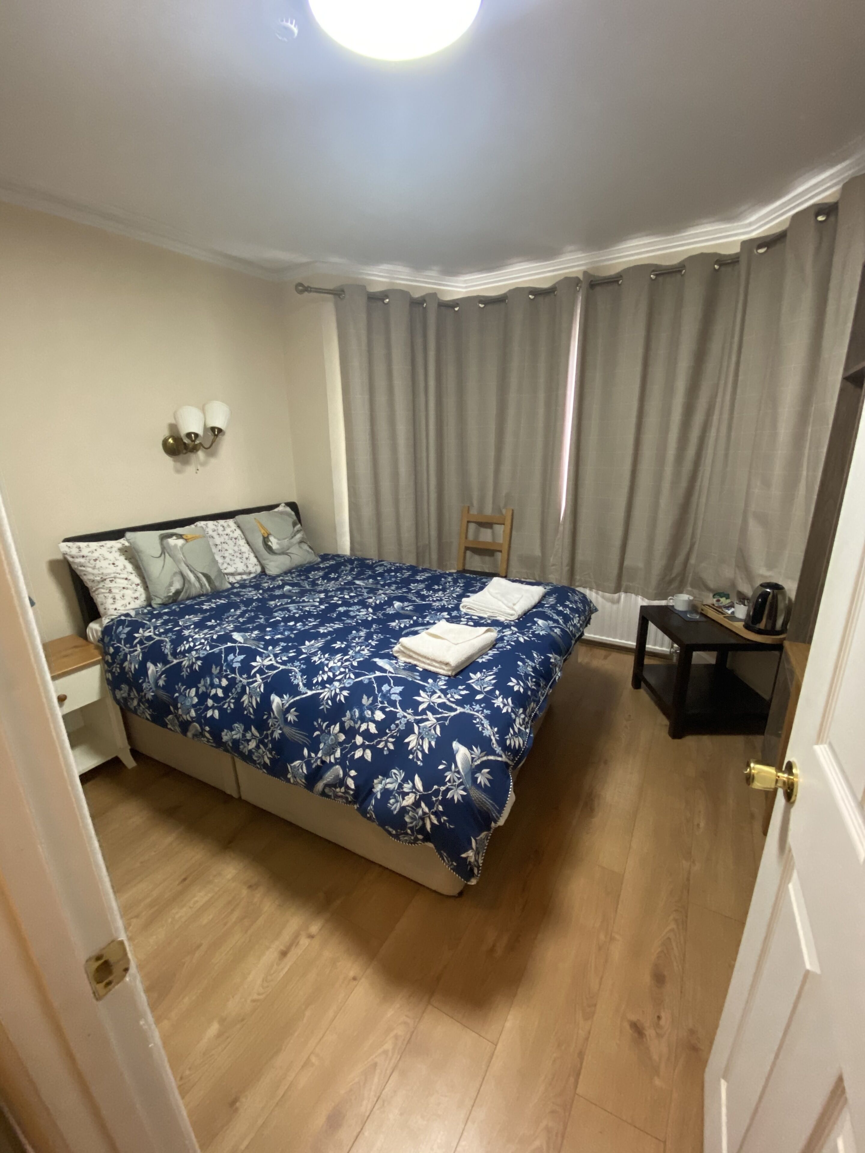 A bedroom with a bed, a nightstand, a chair, a small table, and a curtain.