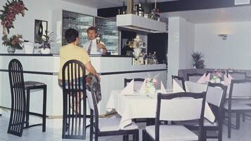 A restaurant interior with a bar area, white tablecloths, and black chairs.