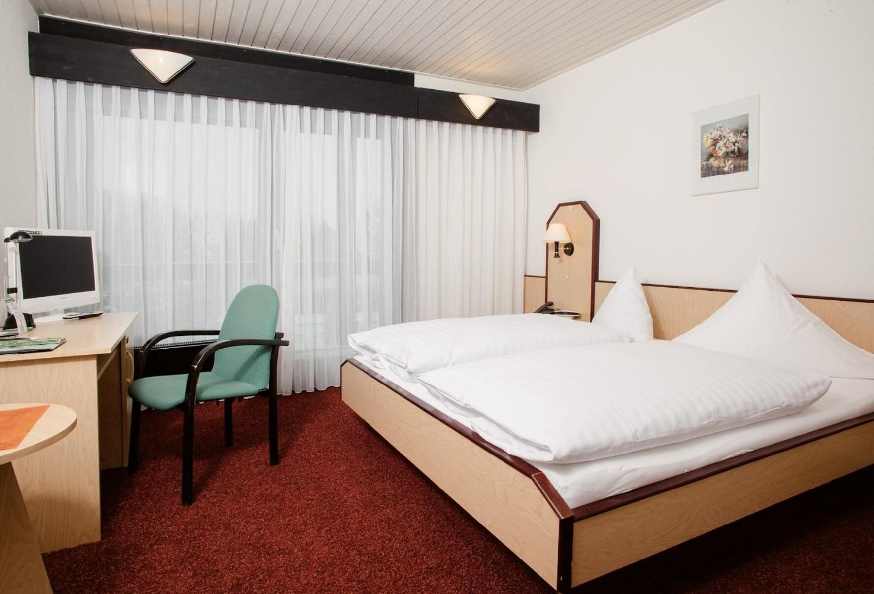 A hotel room with a bed, desk, chair, and a computer.