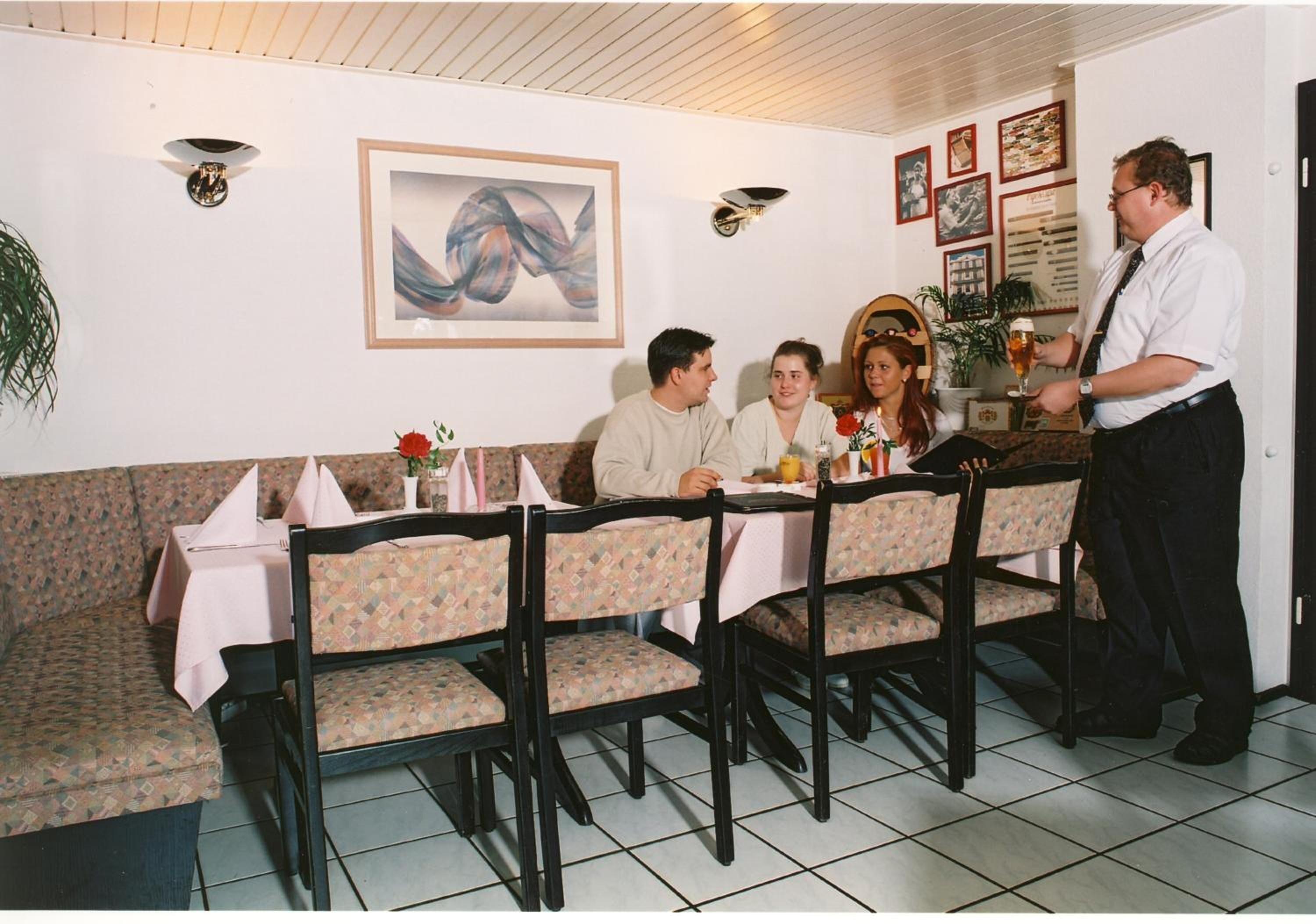 Ein Restaurant mit einer Sitzecke, einem Kellner, der Getränke serviert, und einem Tisch mit einer Blumenarragemement.