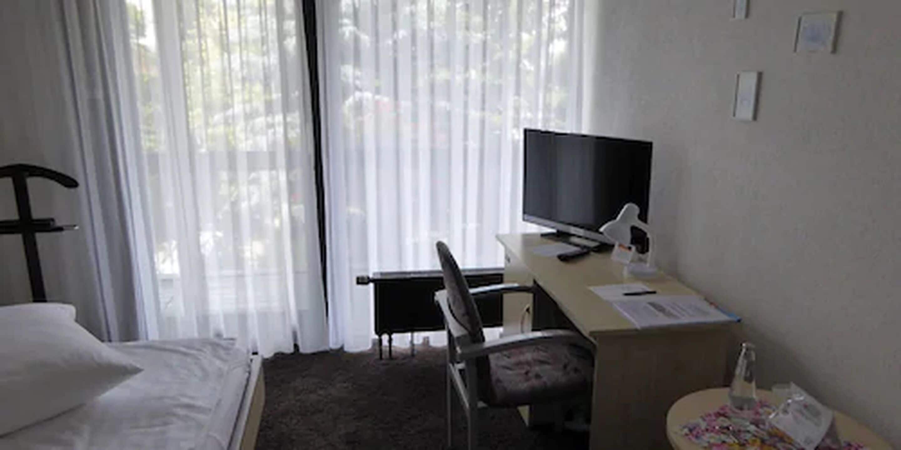 Et hotelværelse med en seng, et skrivebord med en computer, en stol og et fjernsyn.
