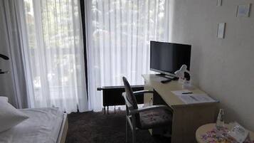 Et hotelværelse med en seng, et skrivebord med en computer, en stol og et fjernsyn.