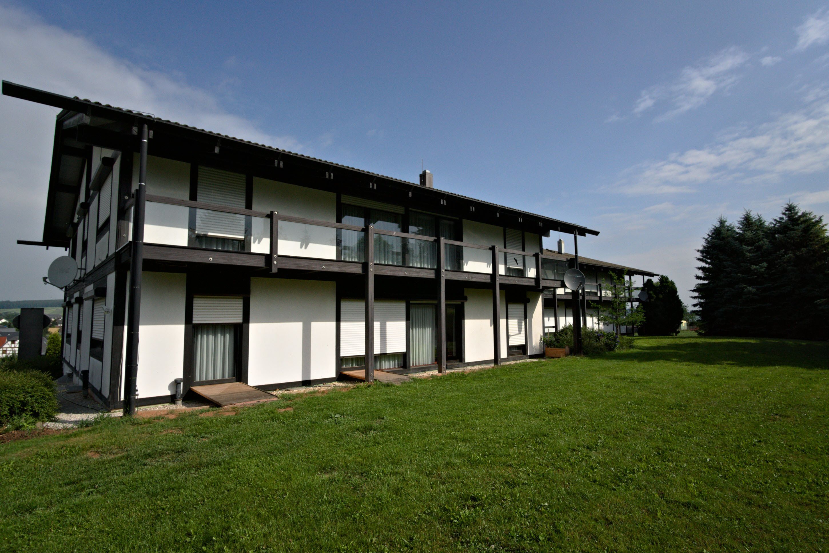 A modern two-story building with a flat roof, large windows, and a covered outdoor area.