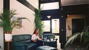 Una habitación con un sofá de cuero verde oscuro, un reposapiés a juego y dos plantas en macetas.