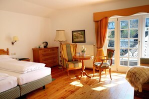 Habitación de hotel con cama, cómoda, mesa con sillas, ventana con cortinas y radiador.