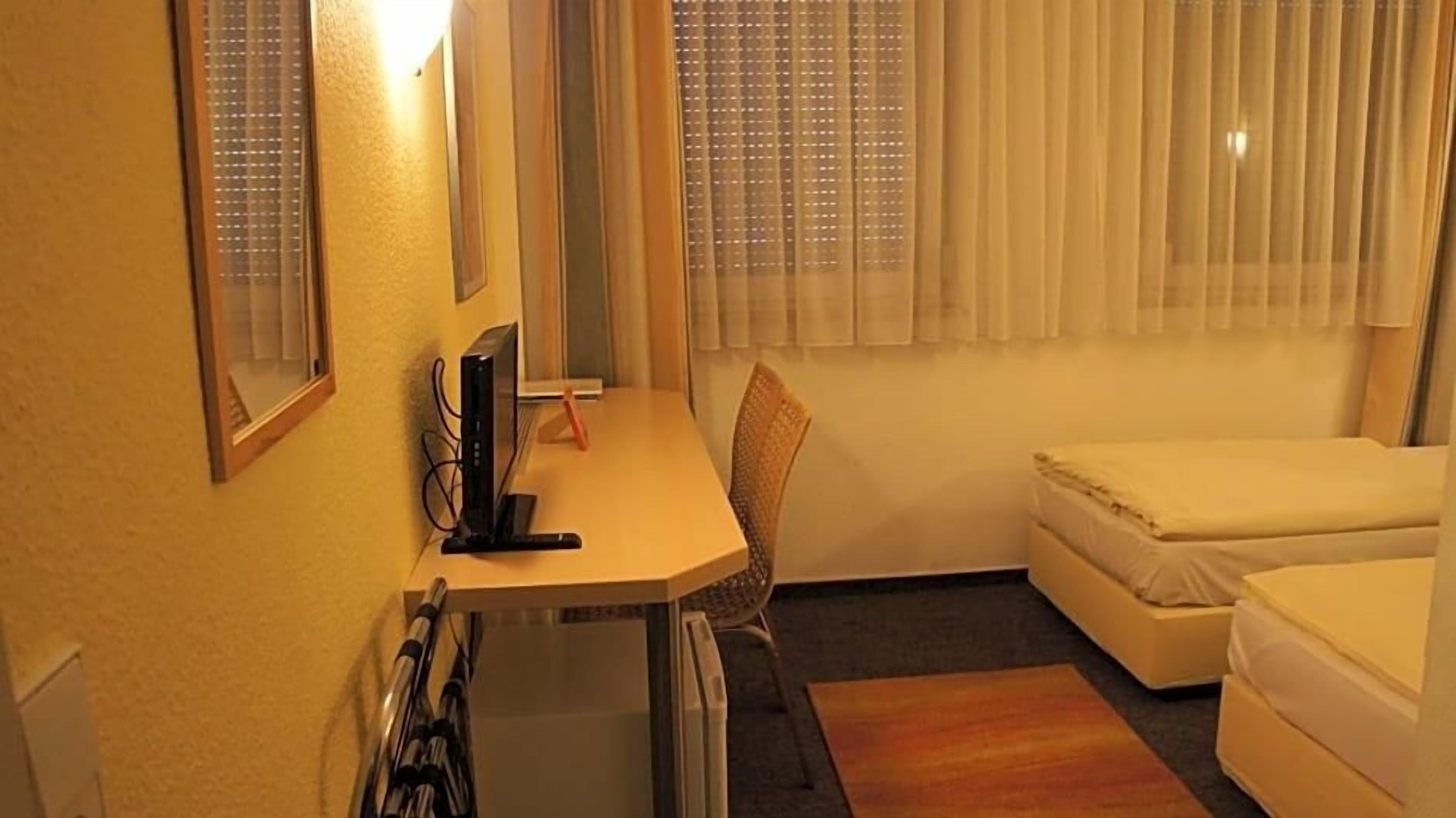Ein kleiner, kompakter Raum mit Schreibtisch, Stuhl und einem Bett.