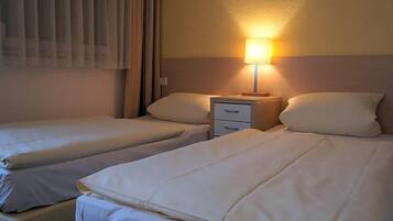 Ein Hotelzimmer mit zwei Betten, einem Nachttisch mit Lampe und einem Fenster mit Vorhängen.
