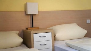 Habitación de hotel con cama, mesita de noche con cajones, lámpara y aplique de pared.