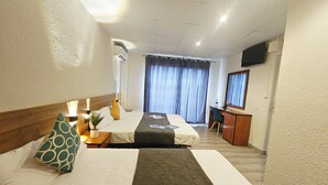 Habitación de hotel con dos camas, un escritorio, una silla, televisión y un gran ventanal con cortinas.