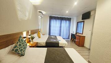 Habitación de hotel con dos camas, un escritorio, una silla, televisión y un gran ventanal con cortinas.