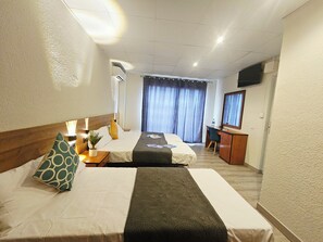 Habitación de hotel con dos camas, un escritorio, una silla, televisión y un gran ventanal con cortinas.