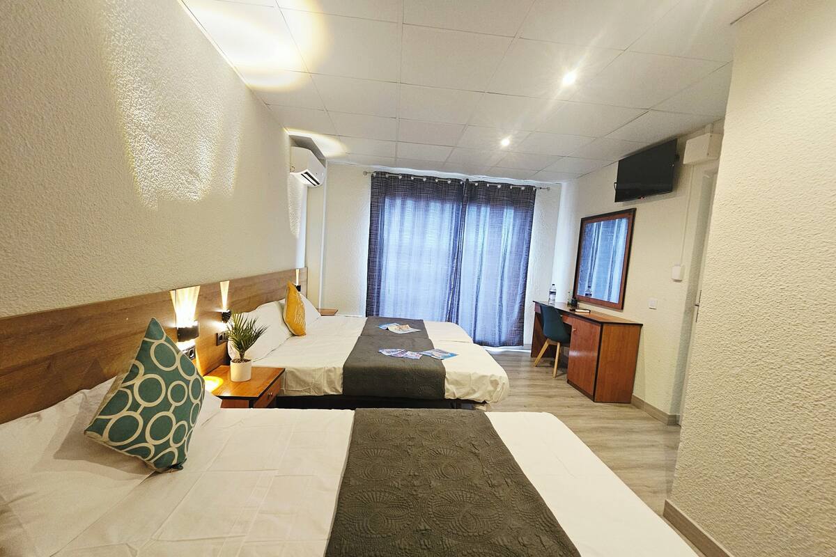 A hotel room with two beds, a desk, a chair, a television, and a window with curtains.