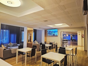 Un moderno vestíbulo de hotel con un área de descanso, una gran pantalla de televisión y una mesa de billar al fondo.