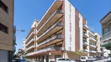Un hotel de varios pisos con balcones, cielo despejado y automóviles estacionados.
