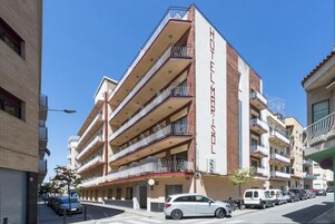 Un hotel de varios pisos con balcones, cielo despejado y automóviles estacionados.