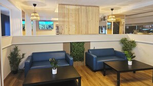 Un hall moderno con sofás azules, un separador de madera y una pantalla de televisión.