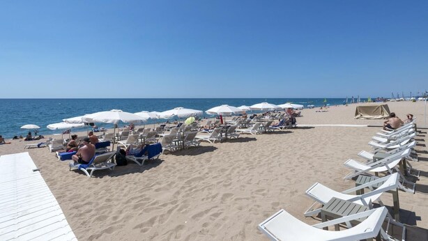 Ein Strand mit Liegestühlen und Sonnenschirmen, ein sandiger Uferbereich und das Meer im Hintergrund.