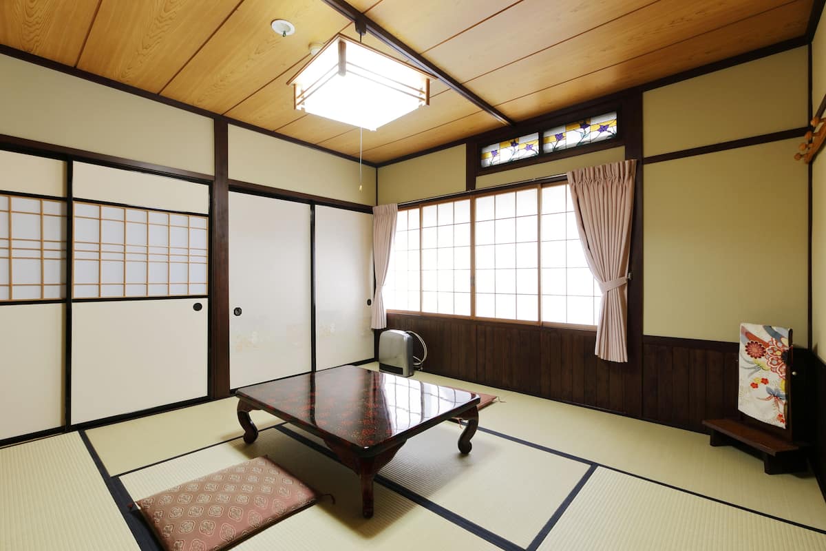 Une pièce de style japonais traditionnel, avec un sol recouvert de tatamis, une petite table en bois, un paravent shoji et une fenêtre avec un rideau.