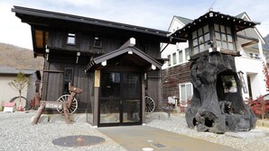 A traditional wooden building with a large wooden wheel and a stone structure resembling a bear's head. - Ryoso Tsuyukusa (Takayama)