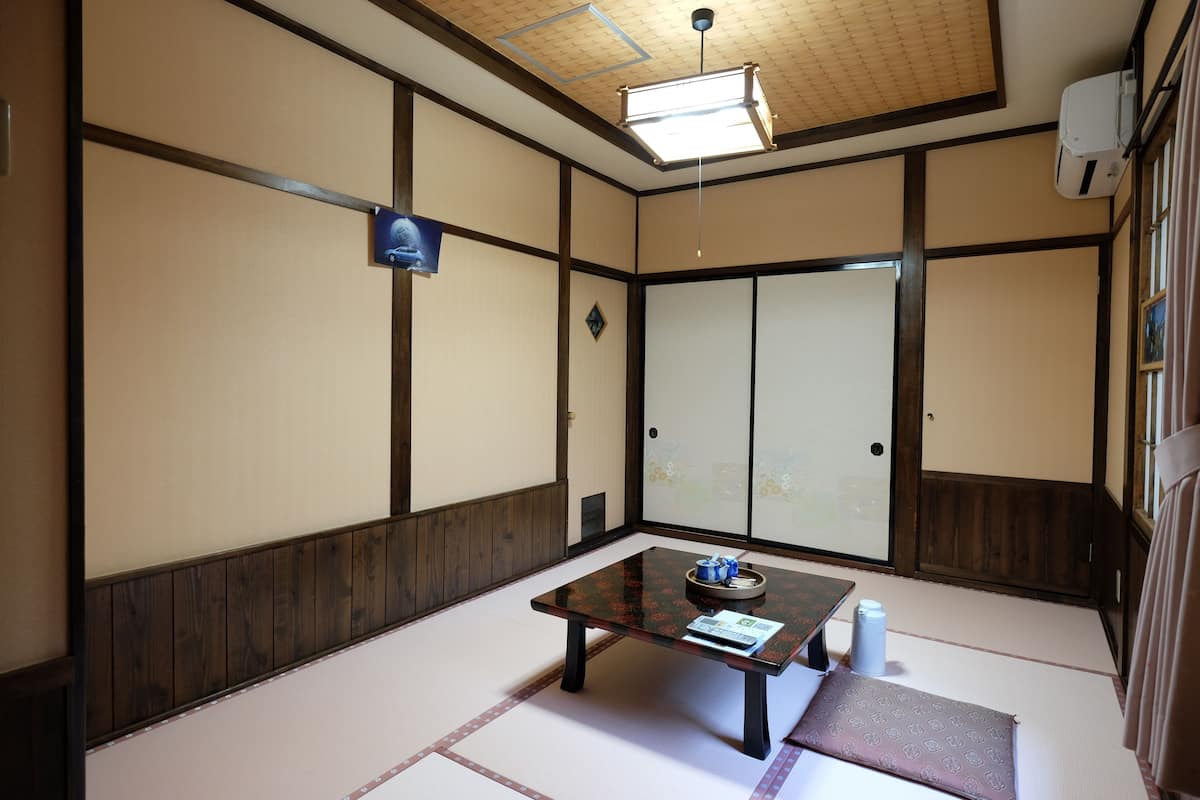 Une pièce de style japonais traditionnel, avec un sol recouvert de tatamis, une petite table basse sur laquelle est posé un plateau, et des portes coulissantes.