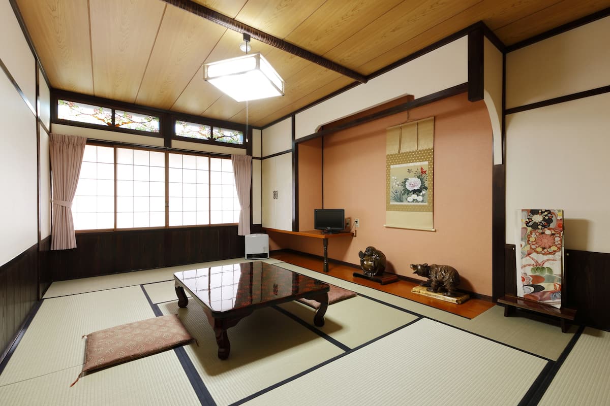Une pièce de style japonais traditionnel, avec un sol recouvert de tatamis, une basse table en bois, un téléviseur et une statue décorative.