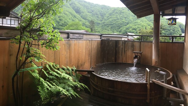 A traditional wooden bathhouse with a large wooden tub, a wooden roof, and a view of lush green mountains. - Ryoso Tsuyukusa (Takayama)