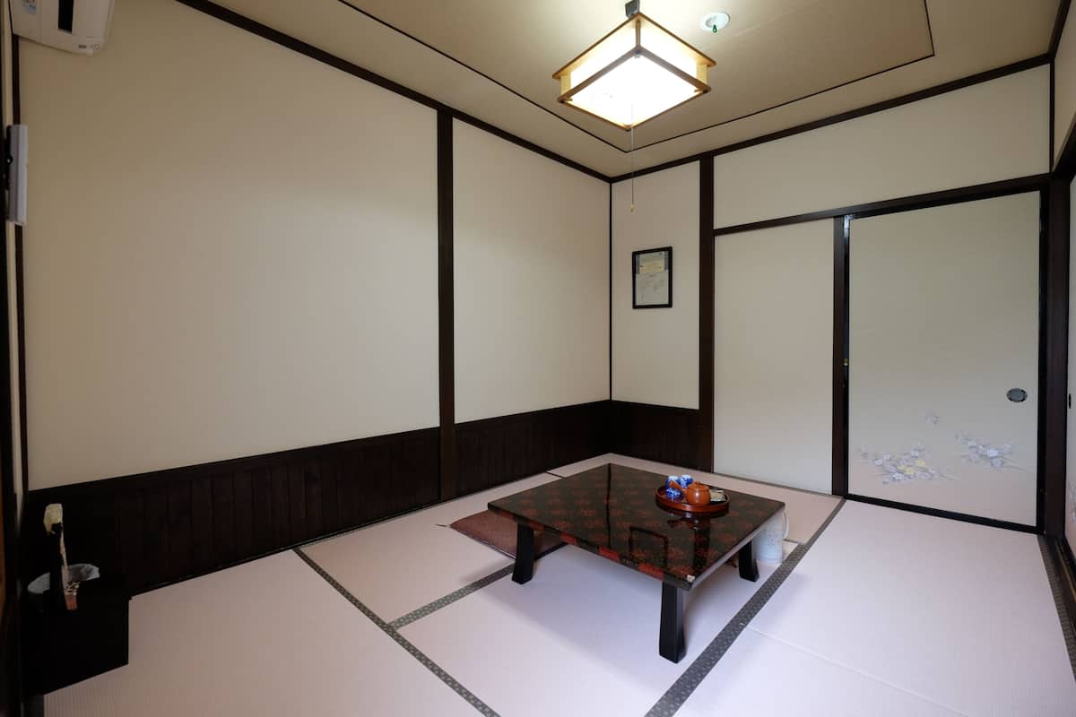 Une pièce traditionnelle avec un sol recouvert de tatamis, une petite table basse, un luminaire suspendu et une porte coulissante.