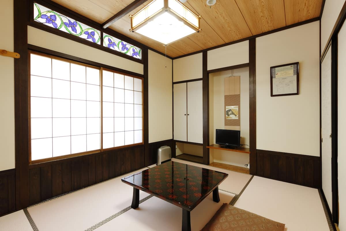 Une pièce de style japonais traditionnel, avec un sol recouvert de tatamis, une table basse, des portes coulissantes et une grande fenêtre ornée de motifs floraux.