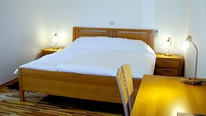 A neatly made bed with a wooden headboard, two bedside tables with lamps, a wooden desk, and a chair. - Villa Molina (Zupa dubrovacka)