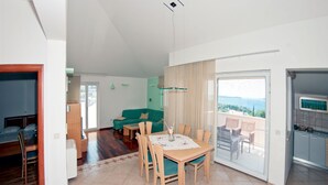 A modern living room with a dining area, a green sofa, and a balcony with a view. - Villa Molina (Zupa dubrovacka)