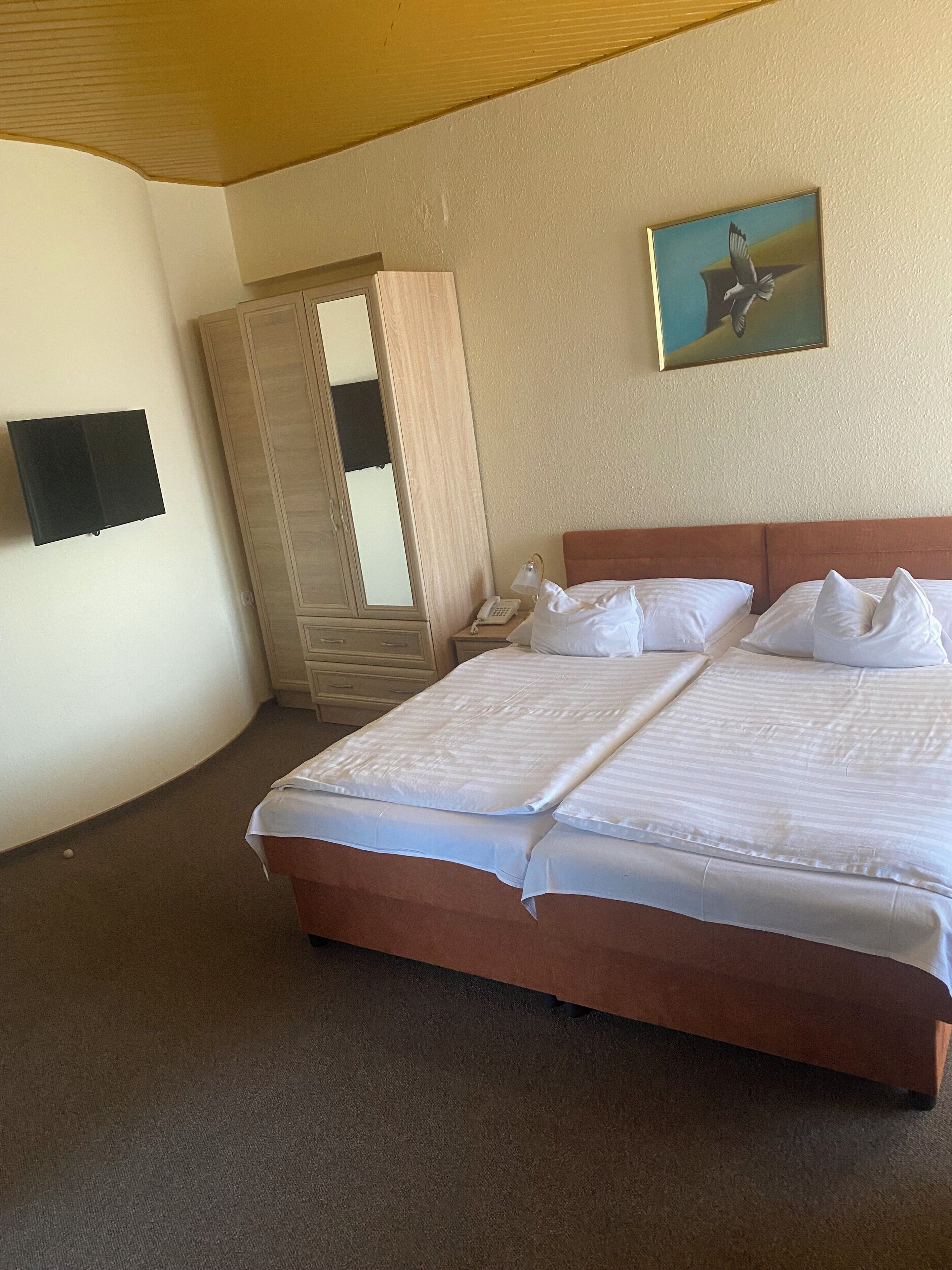 Een hotelkamer met een groot bed, een kledingkast, een spiegel, een schilderij en een telefoon.