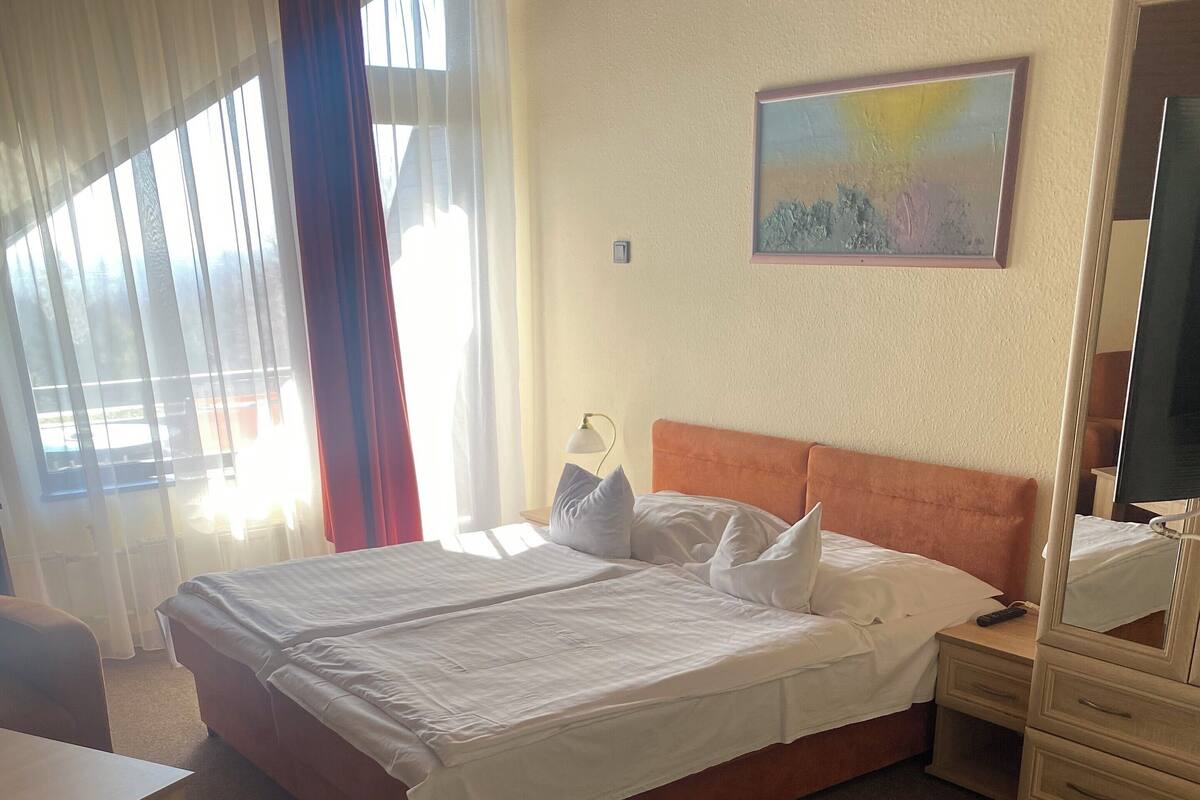 A hotel room with a large bed, a bedside table, a lamp, a dresser, and a painting on the wall.