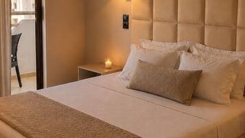 Habitación de hotel con una cama grande, una mesita de noche con lámpara y vistas al balcón exterior.