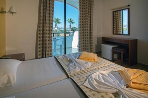 A hotel room with two beds, a desk, a chair, and a view of palm trees and a pool. - Rhodea Mar (Rhodes)