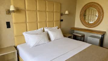 Una habitación de hotel con una cama grande, mesitas de noche, un espejo y un escritorio pequeño.