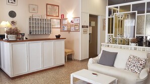 A reception area with a white reception desk, a sofa, and a coffee table. There are framed pictures on the wall, a bulletin board, and a sign that says "Welcome". - Maeva (Lloret de Mar)