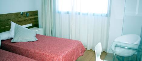 A hotel room with two beds, a glass table, a white chair, and a window with curtains.