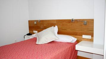 Una cama bien hecha con una colcha roja estampada, una almohada blanca y un cabecero de madera.