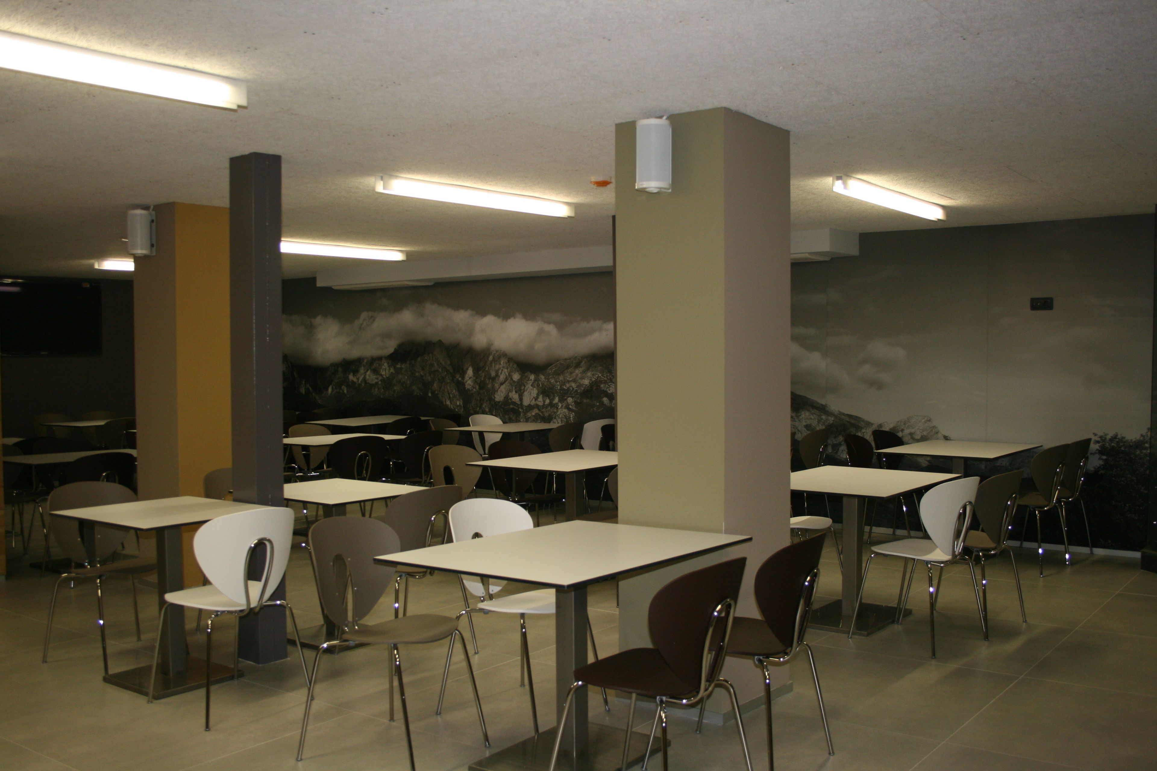 Un comedor con mesas y sillas, un mural en la pared y luces en el techo.
