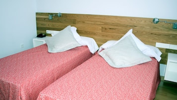 Cama doble con sábanas rojas estampadas y almohadas blancas, cabecera de madera y mesita de noche con una lámpara.