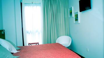 A bedroom with a bed, a chair, a window with curtains, and a wall-mounted TV.