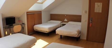 A room with two beds, a desk with a chair, a television, and a skylight.