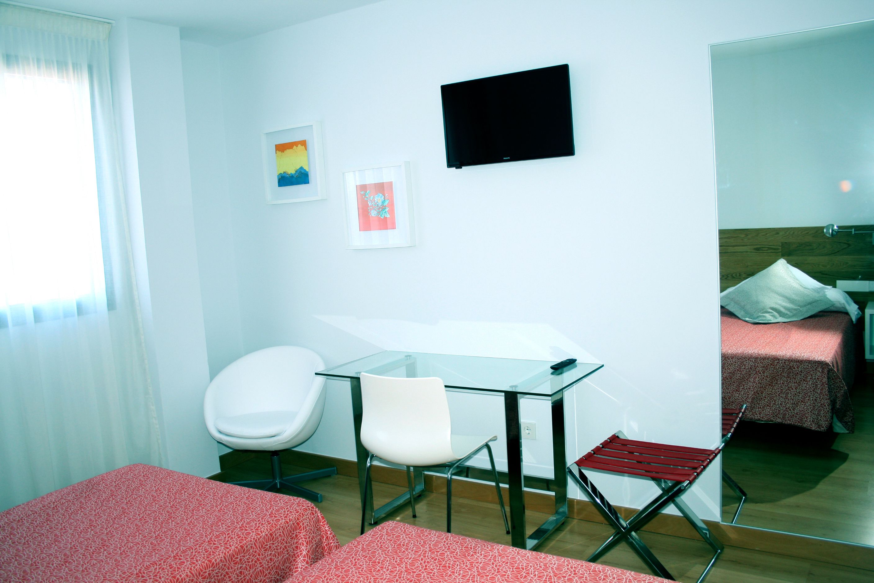 Hotellihuoneessa on lasipöytä, kaksi tuolia, sänky, televisio ja taideteos seinällä.